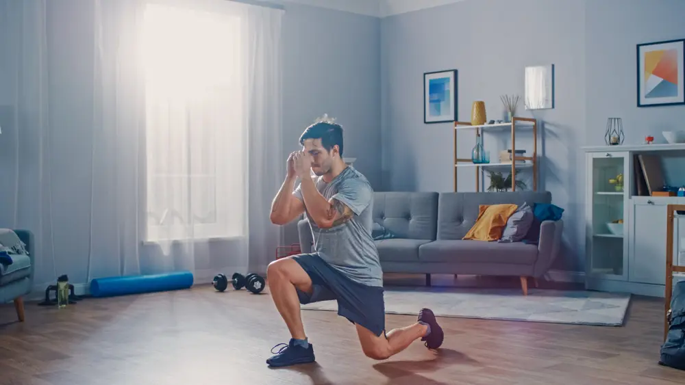 Strong Athletic Fit Man in T-shirt and Shorts is Doing Forward Lunge Exercises at Home 