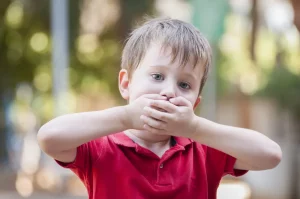 Serious little boy closing his mouth with hands - hiccup