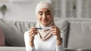 happy glad pretty millennial arab woman in hijab looking at positive pregnancy test in living room interior - symptoms of pregnancy during the menstrual cycle